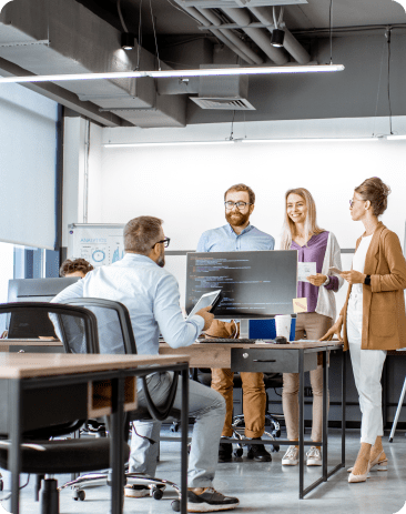 A person at his computer with three people standing across from him