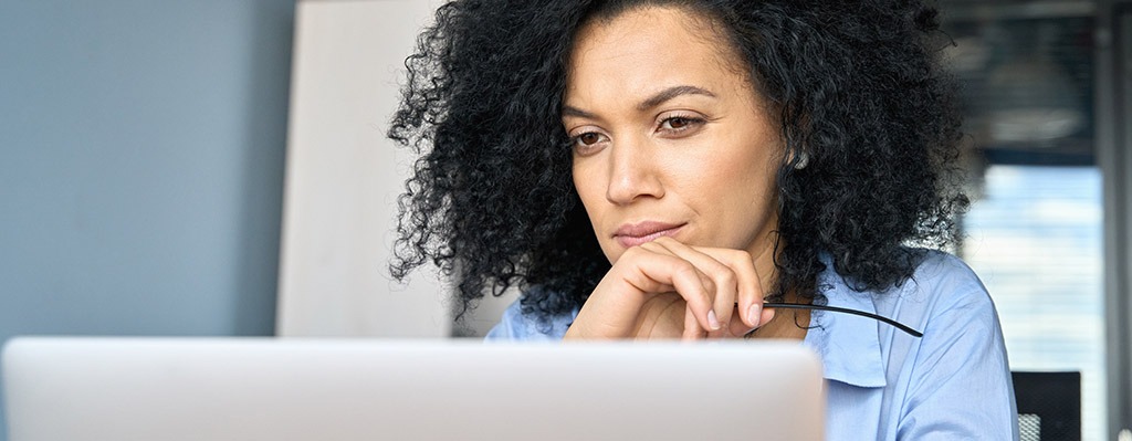 Young serious concerned African American businesswoman sitting at desk looking laptop computer in contemporary corporation office. Business technologies concept. Close up portrait.