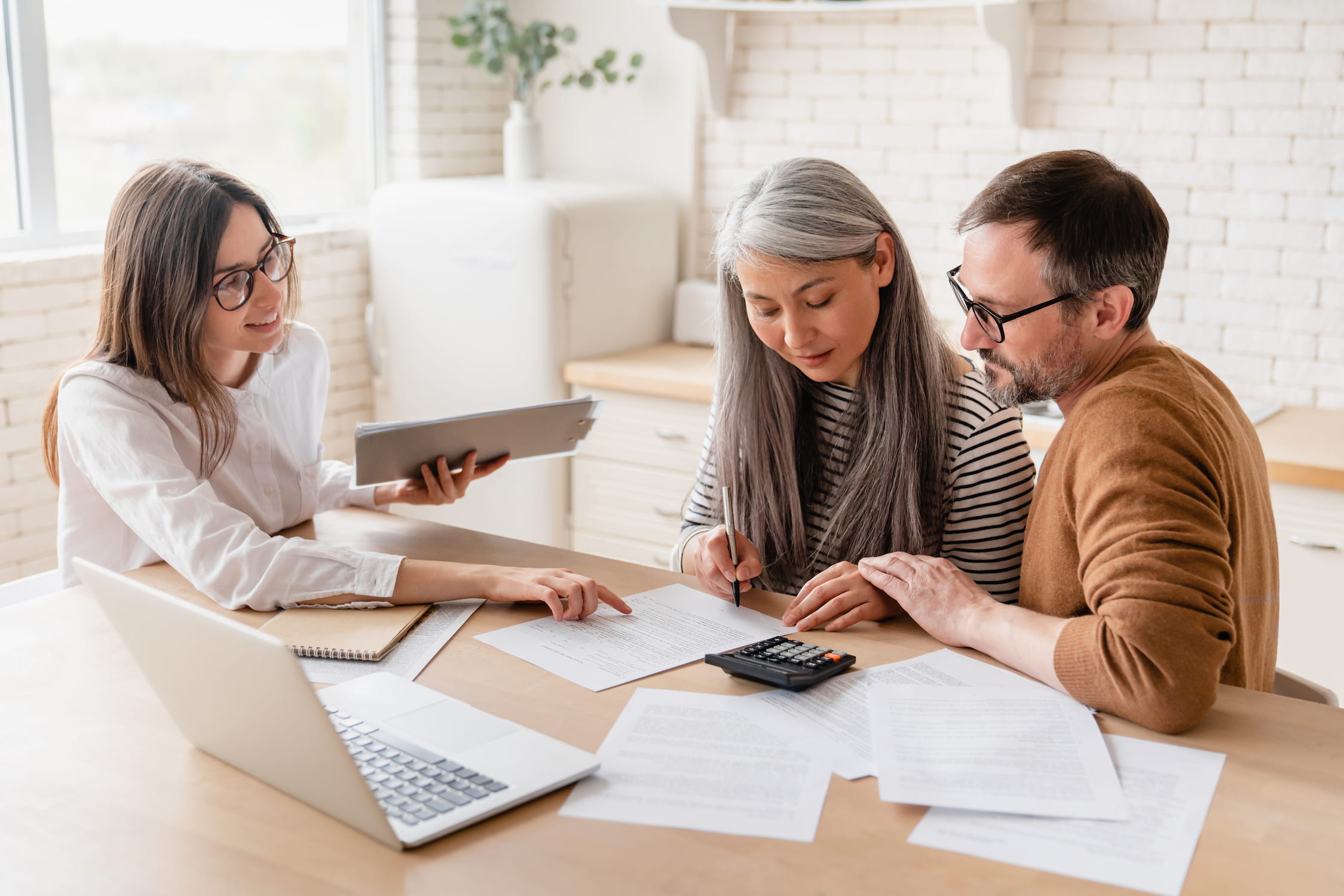 Agent consulting mature family couple, discussing health insurance, signing contract deal of loan pension mortgage at home, calculating funds, investments, savings
